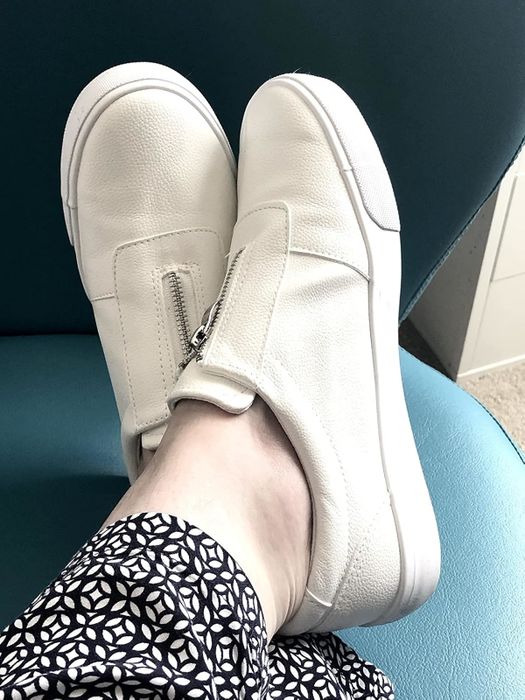 Feet adorned in white slip-on sneakers featuring a side zipper, paired with stylish patterned pants.