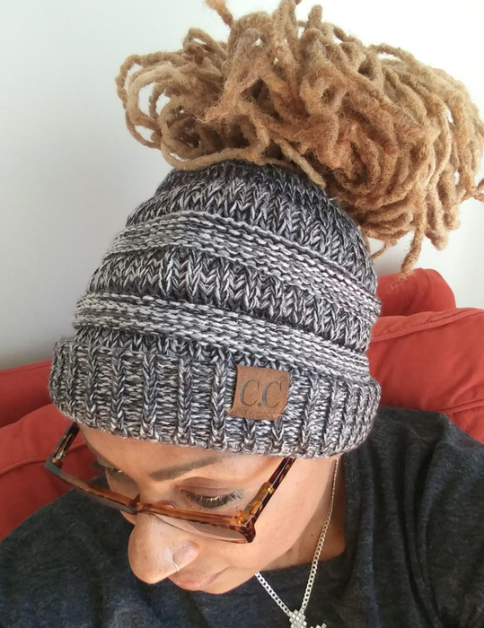 Reviewer showing a top view of a chunky gray knit beanie with a thick bun pulled through it, resting on a red couch