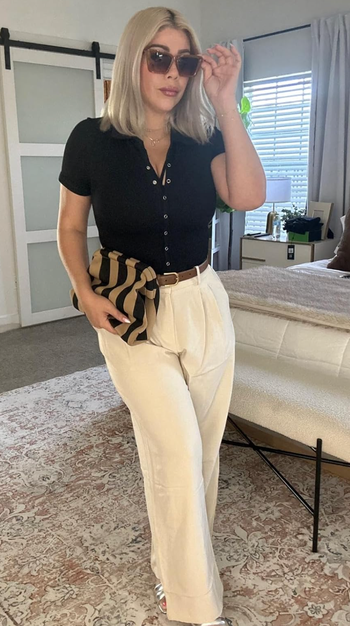 A model wearing a black button-up top paired with white pants.