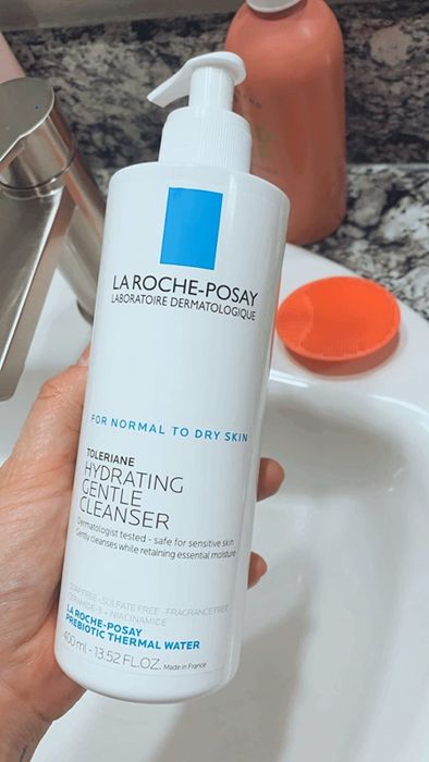 A reviewer holding the cleanser bottle in their hand.