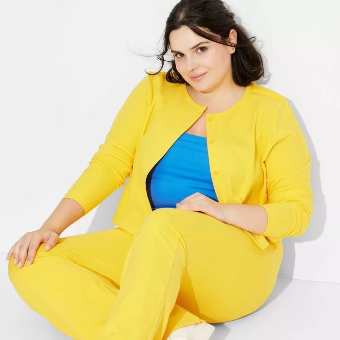 A woman in a bold, bright ensemble relaxes casually; she wears a matching top and pants with a contrasting underlayer. Her fashionable, easygoing pose is perfect for a shopping-related article.