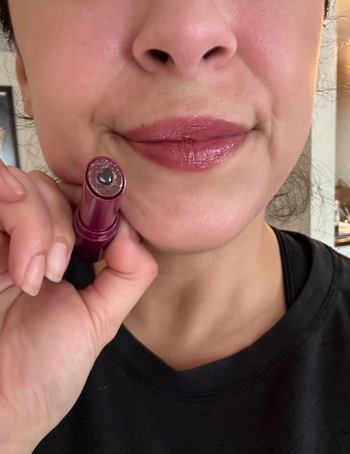 Close-up of lips wearing a shimmery lipstick, with the lipstick tube held near them