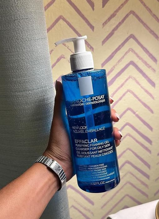 A reviewer holding a bottle of La Roche-Posay Effaclar Purifying Foaming Gel designed for oily skin.
