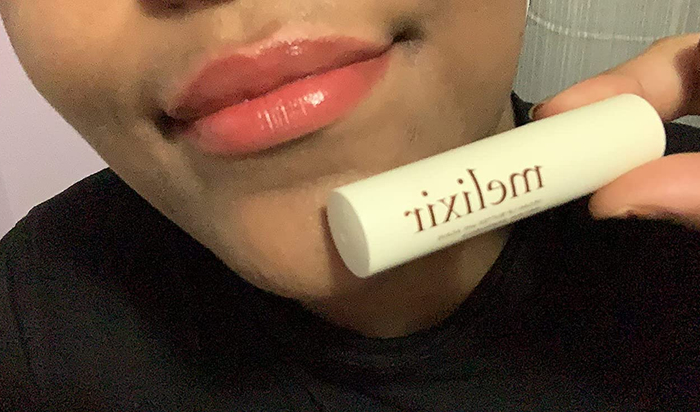 a reviewer applying the lip butter while holding the tube