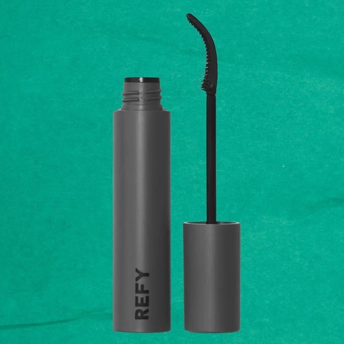 Open gray REFY mascara tube with a curved applicator brush against a green background.