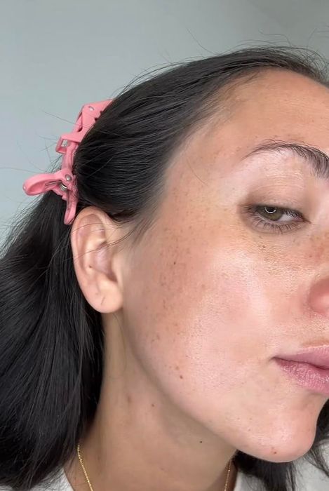 Close-up shot of a person’s face adorned with a pink hair clip, highlighting their clear skin and natural freckles.