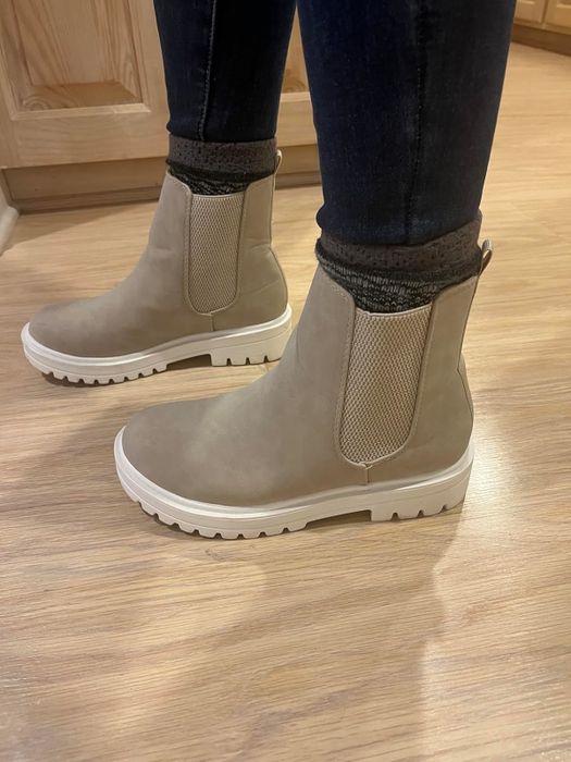 Trendy tan ankle boots featuring textured sides and white soles, paired with black socks and dark pants. Great for casual or fashion-forward outfits.