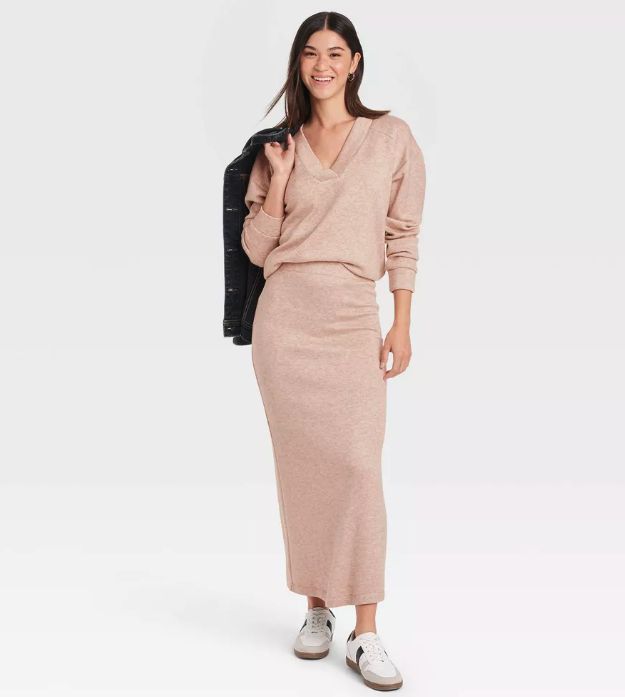 A model is wearing a tan sweater paired with a matching long sweater skirt.