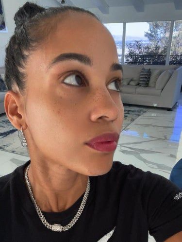 A person gazes thoughtfully upward indoors, wearing strawberry ade lip tint.