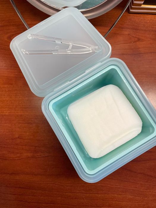 A clear storage container resting on a wooden surface with a neatly folded white towel inside.