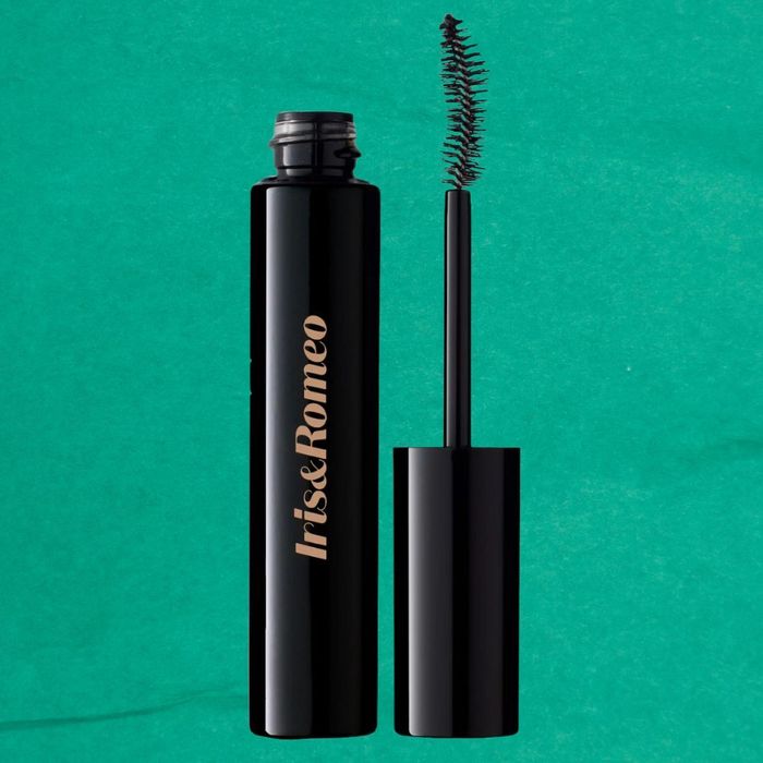 Iris & Romeo mascara with the wand positioned next to the open tube. The mascara is black, and the background is a solid teal color.
