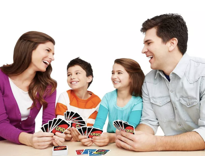 A family of four (two adults, two kids) enjoying a lively game of UNO, smiling and holding cards, creating a warm and engaging family game night vibe.