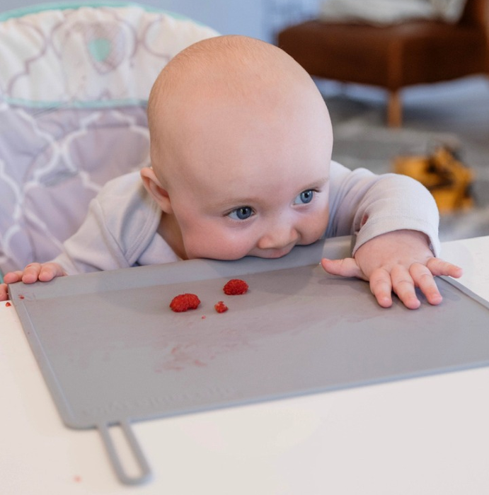 A baby biting the edge of the placemat placed in front of them