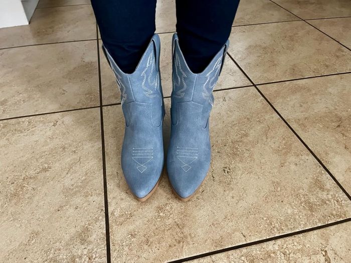 The same reviewer flaunting blue cowboy boots on a tiled floor, paired with dark pants