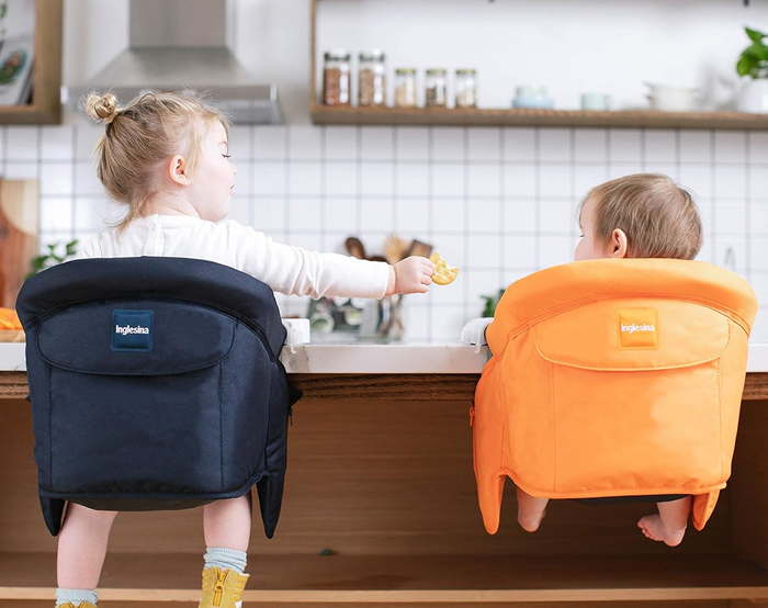 Back view of two toddlers sitting in portable high chairs at a kitchen counter