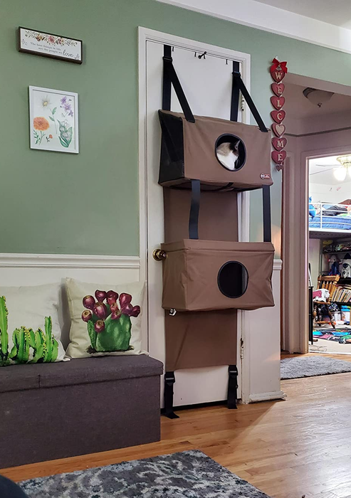 The four-tiered cat condo, featuring multiple entryways and peepholes on various levels, attaches securely to the back of doors with built-in straps