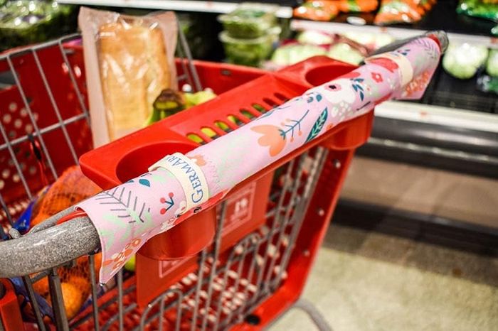 A shopping cart filled with groceries, including bread and oranges, features a decorative handle cover that says 