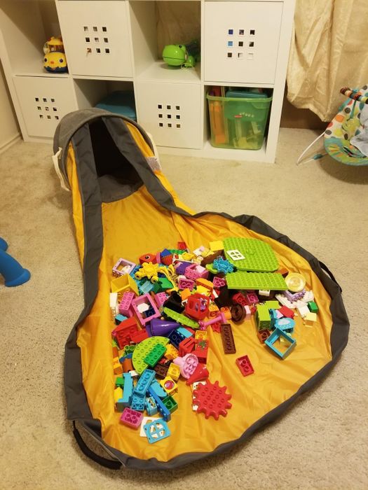 The bag lying flat with the mat spread open, toys scattered on top