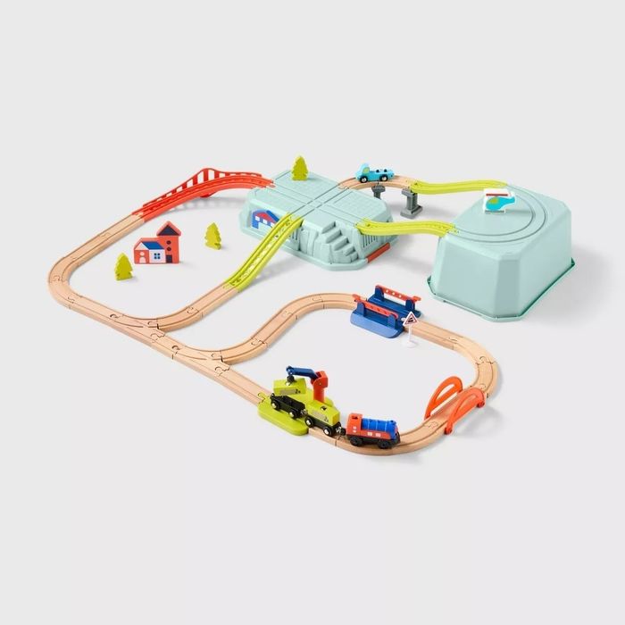 A toy wooden train set complete with tracks, bridges, and buildings such as a house, a station, and trees — all the essentials for a complete miniature world.