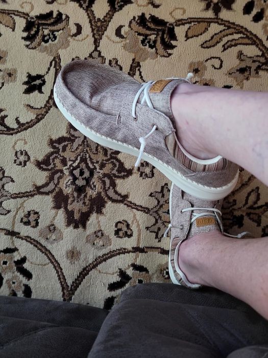 A reviewer’s feet in light, textured slip-on shoes with white laces, resting comfortably on a patterned rug.