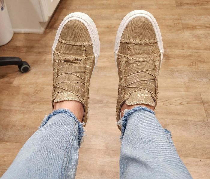A reviewer casually rests their feet, wearing frayed denim jeans and distressed sneakers, showcasing a laid-back shoe style