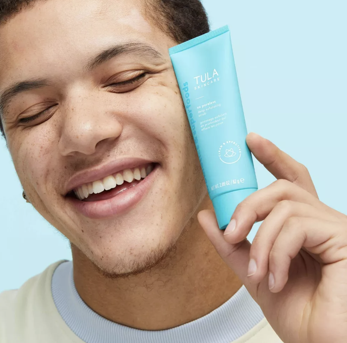 Model holding a tube of exfoliating scrub