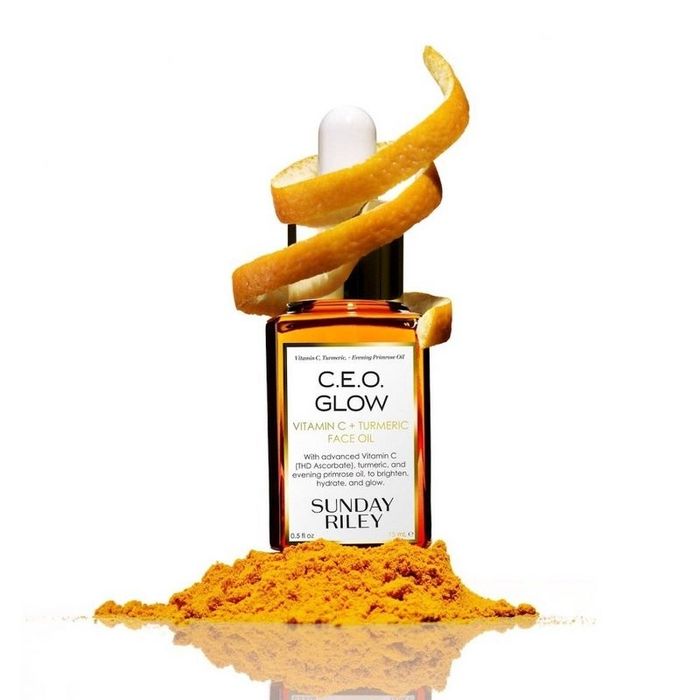 A bottle of facial oil with a small mound of turmeric next to it