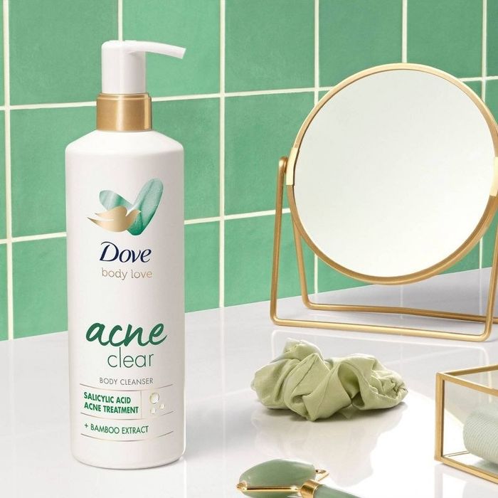 A bottle of acne-fighting body wash, a green scrunchie, a jade roller, and a mirror