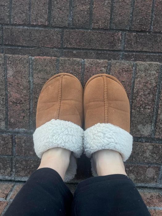 A reviewer showcasing cozy shearling-lined slippers, comfortably resting on brick steps, evoking a sense of relaxation and home comfort for a shopping guide on indoor footwear.