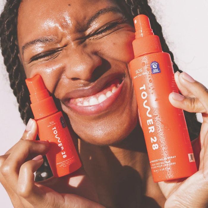 Model holding two orange bottles of the facial spray.