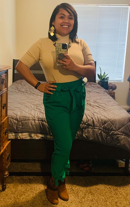 Reviewer dressed in a beige top, green high-waisted trousers, and brown boots.
