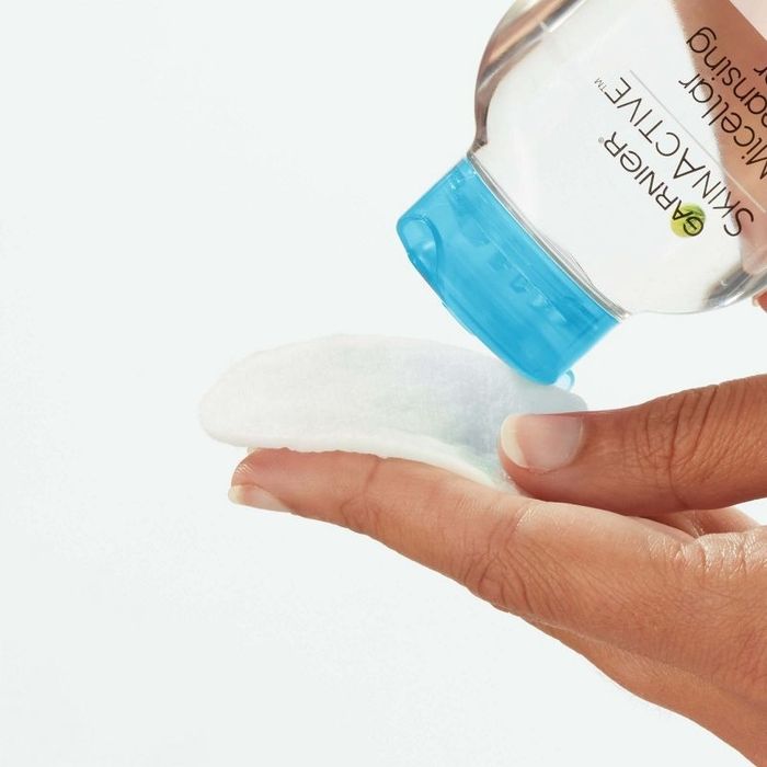 A person dispensing micellar water onto a cotton pad