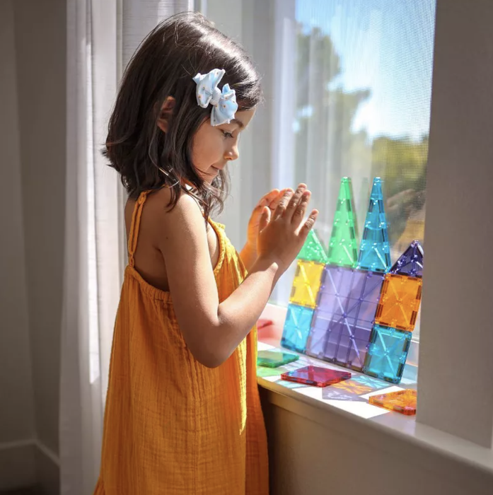 A child has fun with colorful magnetic building tiles on a windowsill.