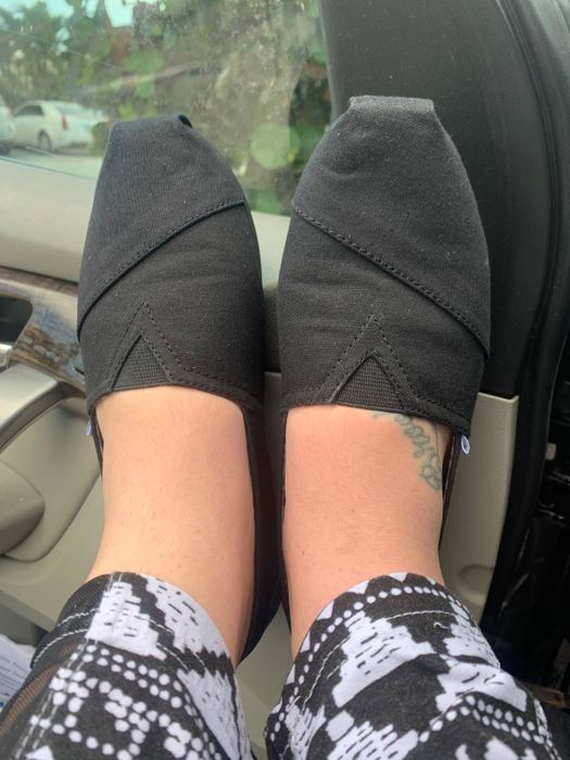 A reviewer rocking black slip-on shoes with a geometric pattern, sitting in a car with pants featuring a black and white abstract design.