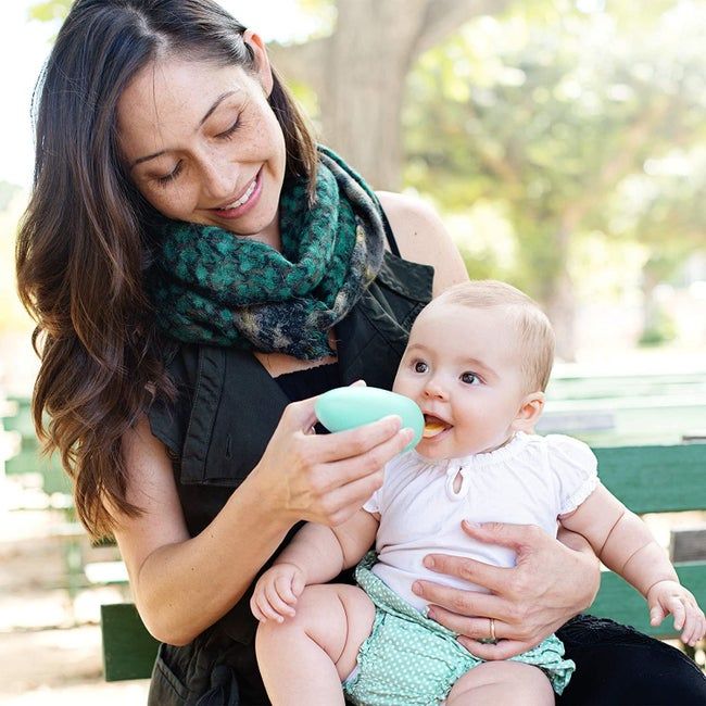 A parent feeding an infant on a park bench with the food storage spoon