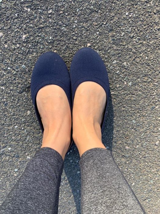 A reviewer wearing textured flat shoes and gray leggings, seen from above while standing on pavement.