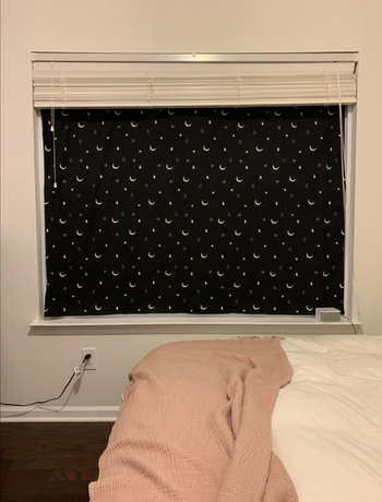 A blackout curtain featuring white moons and stars, suctioned to a window, effectively blocking out light