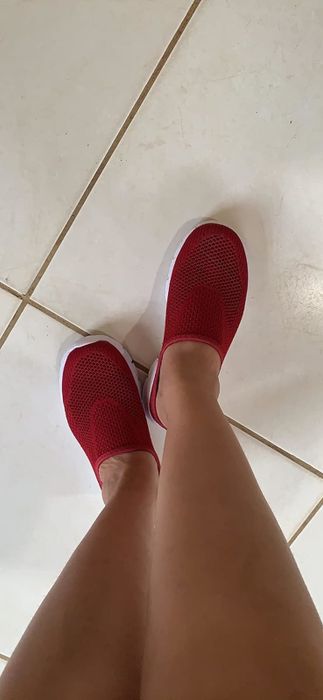 A reviewer rocking red slip-on sneakers, standing on a tiled floor.