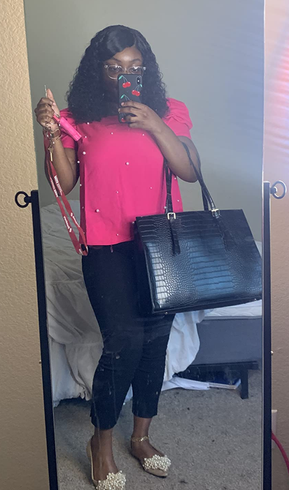 A person in a chic outfit posing for a mirror selfie, wearing a bold top, fitted pants, stylish handbag, and embellished shoes