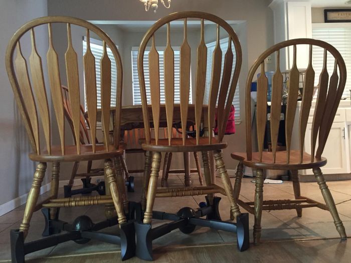 The black booster seat placed under two chairs, demonstrating the height it adds compared to a chair without the booster