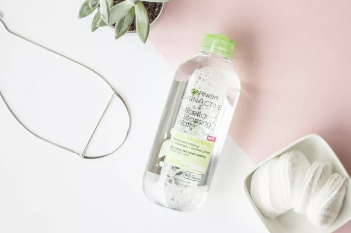 A bottle of micellar water placed next to a tray of cotton rounds