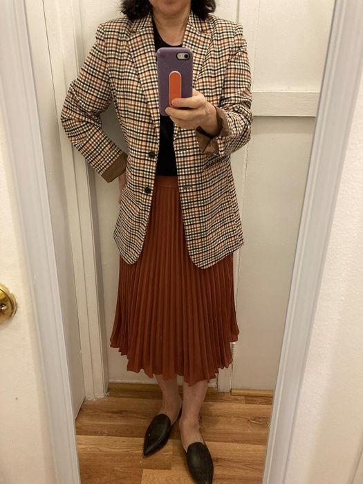 Person dressed in a plaid blazer, pleated skirt, and loafers, creating a stylish yet professional look.