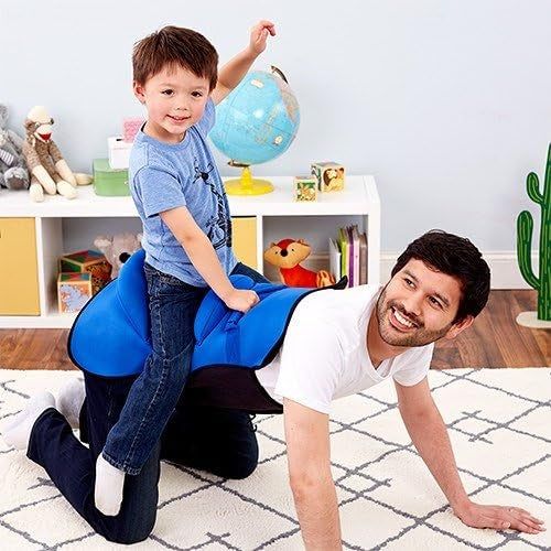 A child is seated on the back of an adult (likely their parent) while playing indoors. The background features toys and a globe.