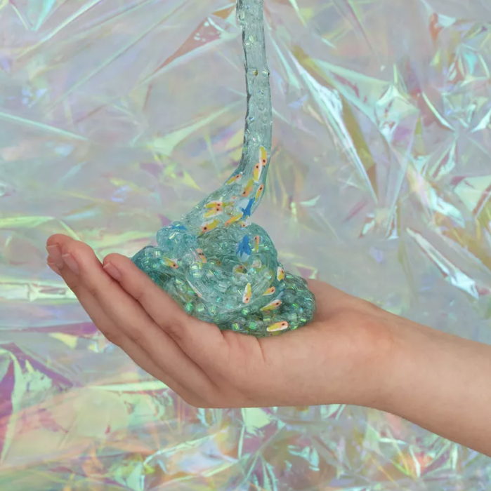 Glittery slime with colorful sprinkles flows over an open hand, set against a holographic background.