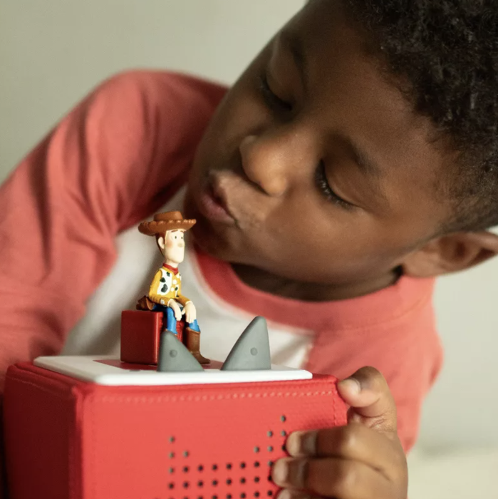A child plays with a Woody toy figure on a red audio device.