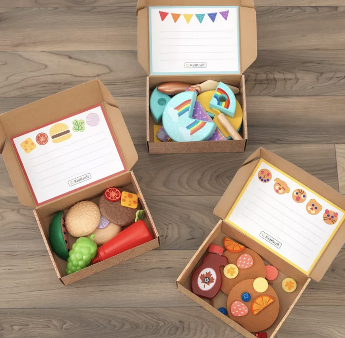 A collection of three Kraftando DIY kits laid out on a wooden surface: a burger-themed kit, a rainbow kit, and a cookie decorating set.