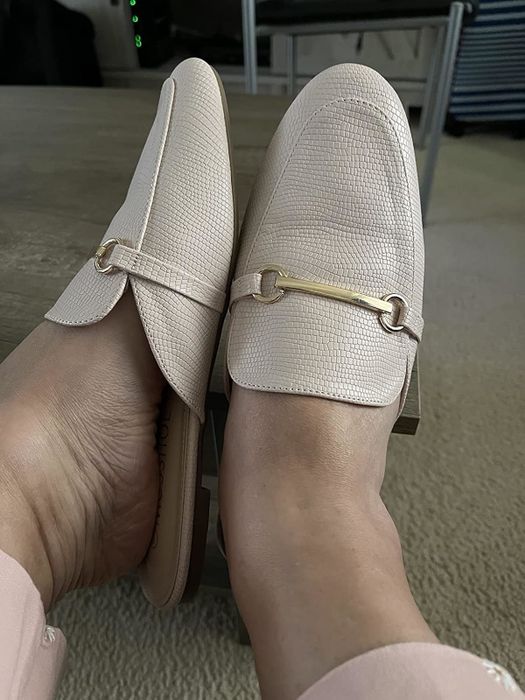 A reviewer wearing loafers with a textured finish and gold buckle detail, shown resting on a carpeted floor