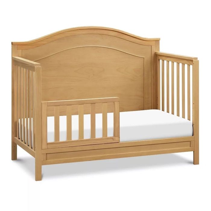Wooden toddler bed with a safety rail and curved headboard. Perfect for a child's room.