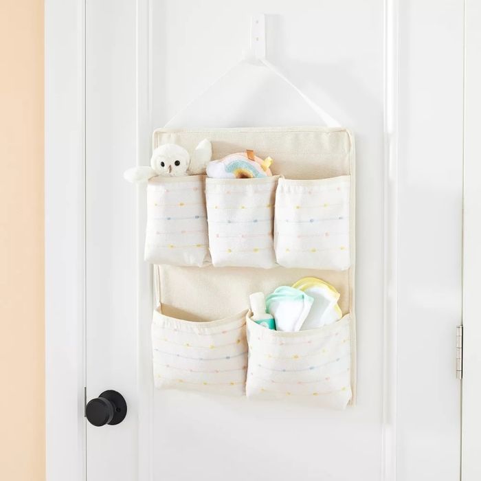 A fabric hanging storage unit with multiple pockets filled with baby necessities, hung on a door.
