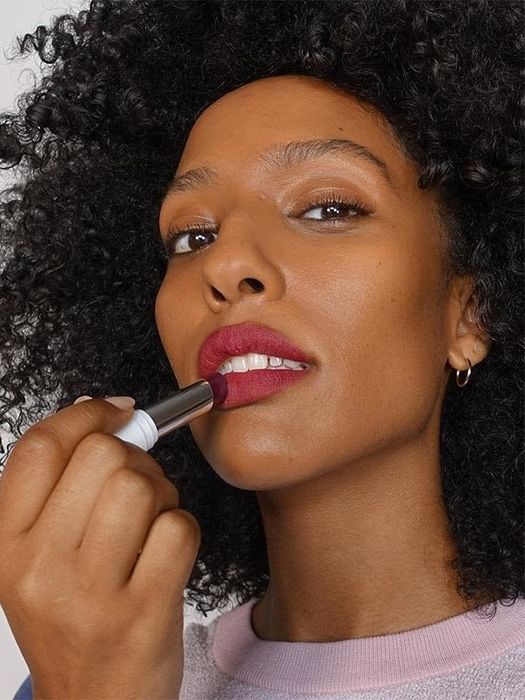 A model applying berry-colored lipstick to their lips